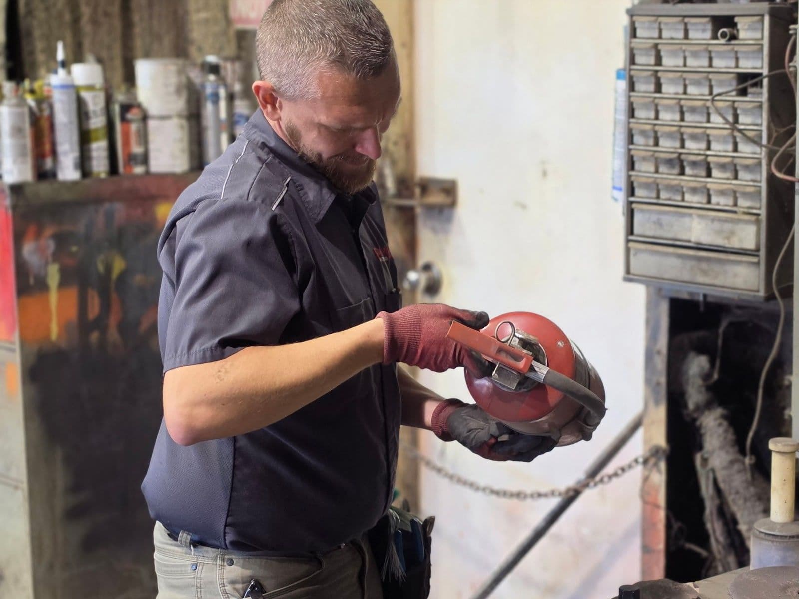 First-Line technician checking the valve and pressure gauge on a fire extinguisher in an industrial shop