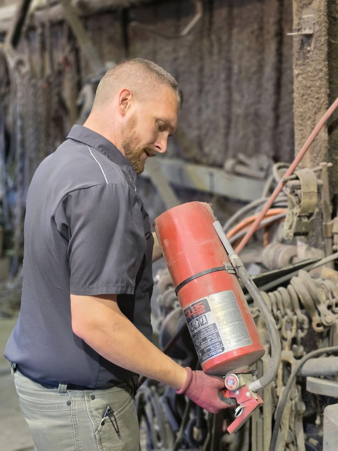 First-Line technician checking a hose-type fire extinguisher in a heavy-equipment shop