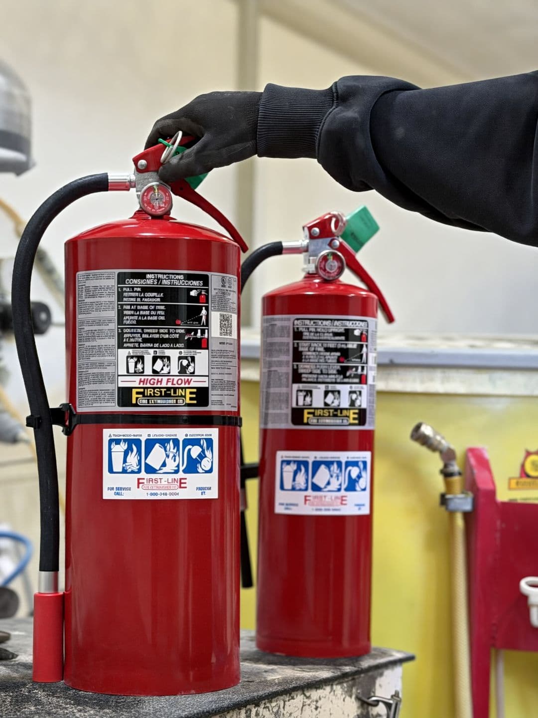First-Line technician checking the valve on two red fire extinguishers in the shop