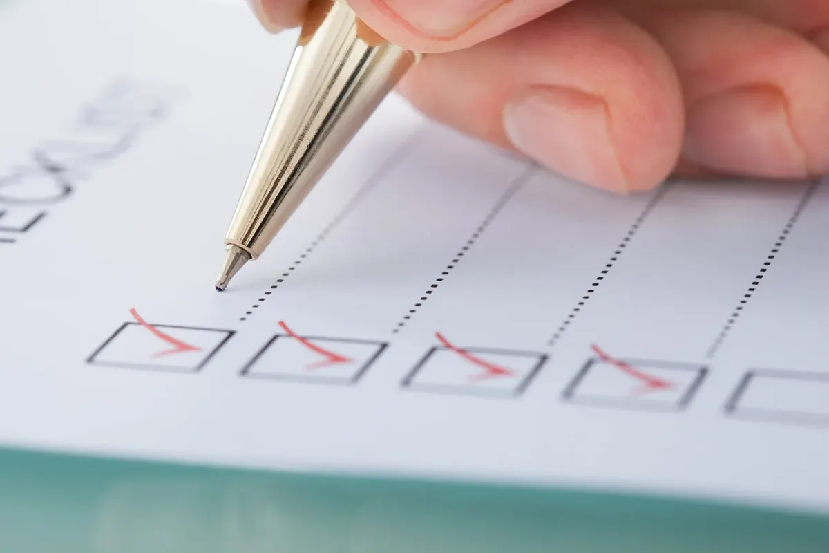 A hand with a pen checking off boxes on a printed checklist