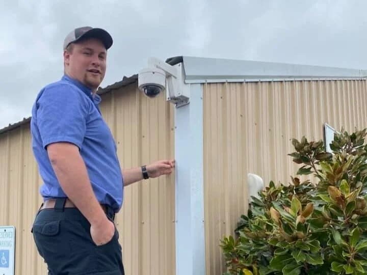 First-Line technician at the shop with a white outdoor security camera on the eave